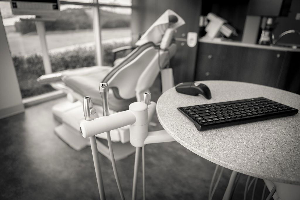 The image shows a dental office with a computer desk, keyboard, mouse, and a dental chair with a headrest and instruments attached to it.