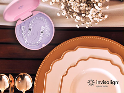 The image shows a collection of tableware items including plates, bowls, and a cake stand, along with a small box with an intricate design, set against a wooden surface with a pink lid visible in the background.