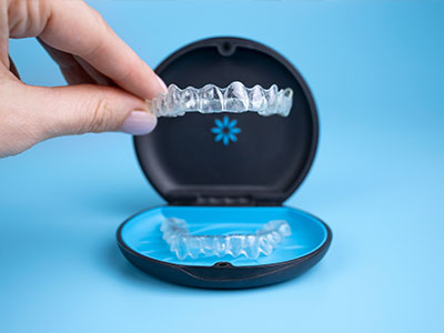 The image shows a person s hand holding an open dental impression tray with a blue base against a light blue background, indicating the display of a dental appliance for viewing or demonstration purposes.