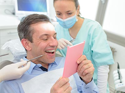 A man holding up a pink card with his mouth open while surrounded by dental professionals, likely in a dental office setting.