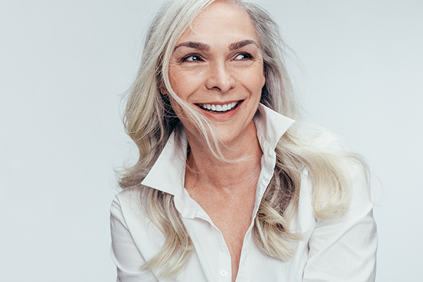 A woman with gray hair smiles at the camera, set against a white background.