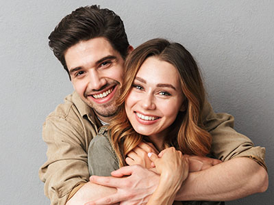 A man and woman hugging each other with smiles on their faces, posing for a portrait-style photograph.