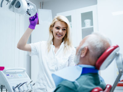 A dental hygienist assisting an elderly patient with dental treatment, both wearing protective face masks.