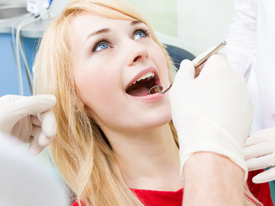 A woman receiving dental care with a dentist performing a procedure on her teeth while she smiles.