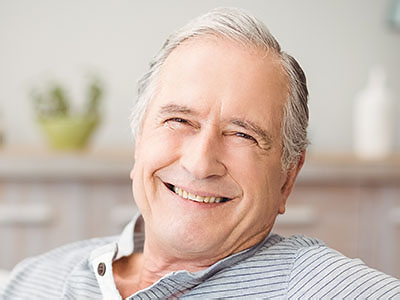 An elderly man with white hair, wearing glasses, sitting comfortably in a chair with a smile on his face.